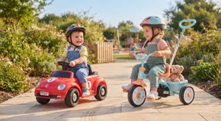 Deux tout-petits dans un jardin, l'un sur un porteur Coccinelle rouge, l'autre sur un tricycle évolutif, guide de la voiture électrique bébé 1-2 ans
