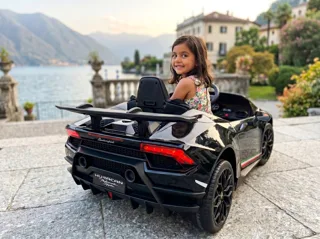 Lamborghini Huracán électrique enfant 12V noire, petite fille au volant au bord d'un lac italien, trois-quarts arrière