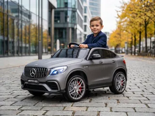 Mercedes GLC 63 AMG 12V gris mat, enfant souriant au volant sur une place urbaine, trois-quarts avant
