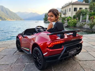 Lamborghini Huracán électrique enfant 12V rouge, petite fille au volant au bord d'un lac italien, trois-quarts arrière