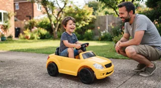Jeune enfant ravi au volant d'une petite voiture jaune à conduire dans le jardin, son père souriant à ses côtés, illustration du guide budget voiture électrique enfant pas cher