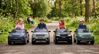 Quatre Range Rover électriques pour enfant alignés dans un parc : Evoque bleu, Velar gris, Sport noir et Vogue vert, avec enfants au volant, illustration du guide Quel Range Rover enfant choisir