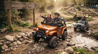 Deux enfants à bord d'un 4x4 électrique orange franchissant un chemin boueux et rocailleux tout-terrain, un autre 4x4 en arrière-plan, guide du 4x4 électrique enfant
