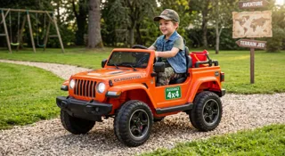 Enfant en casquette au volant d'une Jeep Gladiator électrique orange 12V sur un chemin de gravier, panneaux aventure en arrière-plan, illustration du guide Jeep Gladiator enfant pickup 4x4